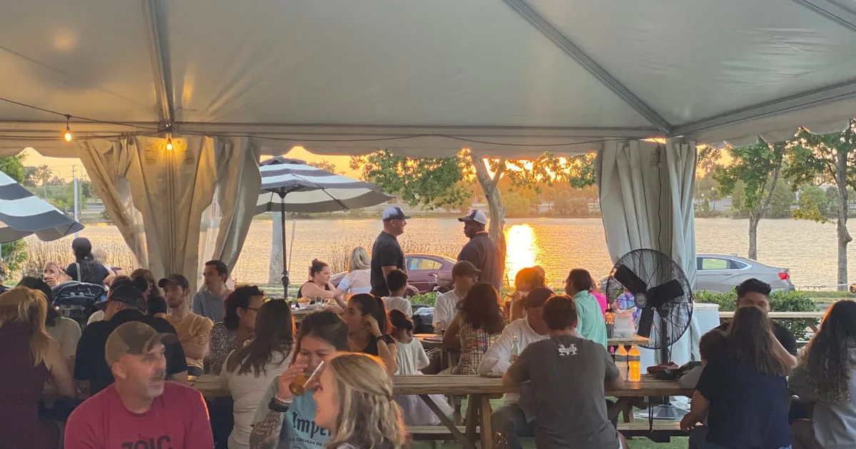 Covered patio at Swan Brewing packed with guests at picnic tables, Lake Wire glowing at sunset in the background