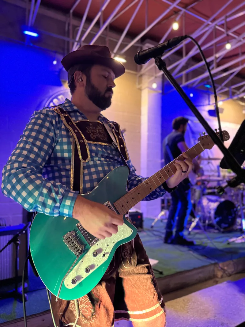 Guitarist performing on the indoor stage at Swan Brewing under blue stage lighting