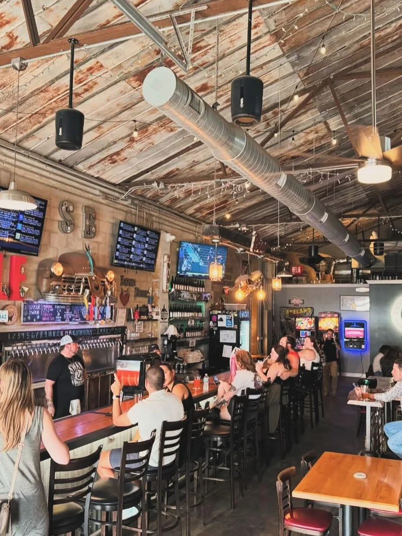 Swan Brewing taproom interior — full bar with tap handles, exposed ceiling, guests seated along the bowling alley bar