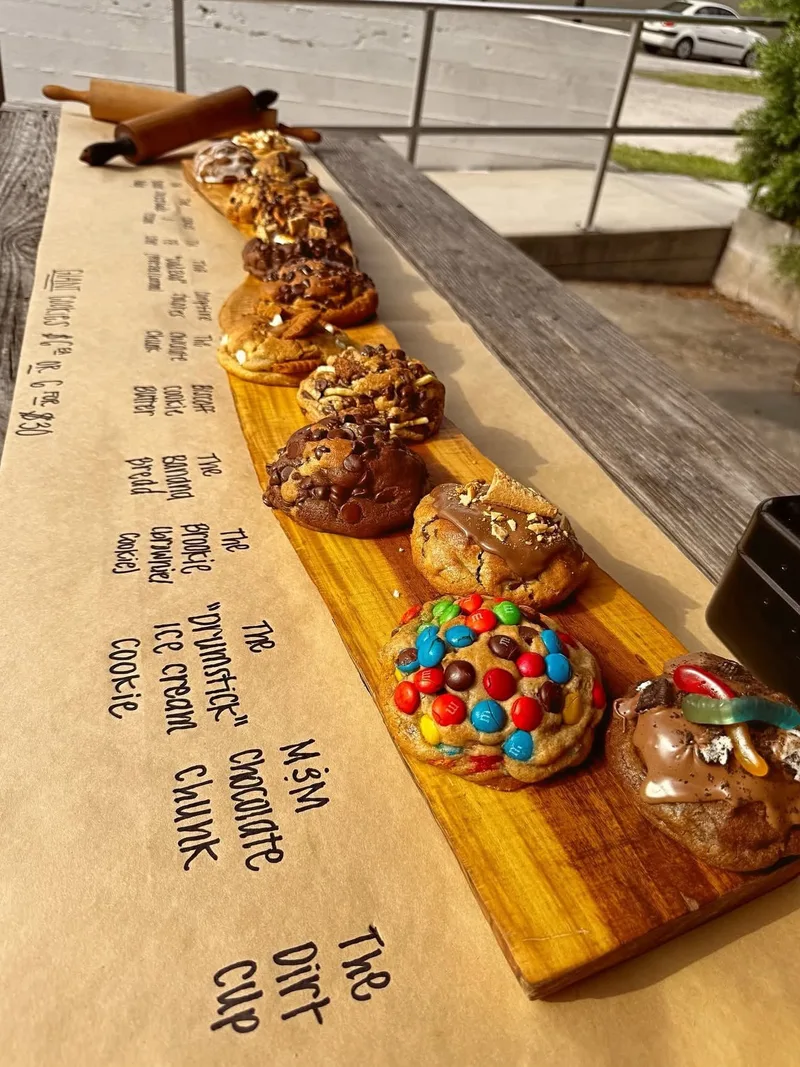 Close-up of The Rolling Pin's gourmet cookie display — M&M, chocolate chunk, dirt cup, and more on a wooden board